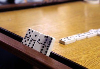 A close-up of hands placing domino tiles on a wooden table with focused players in the background.