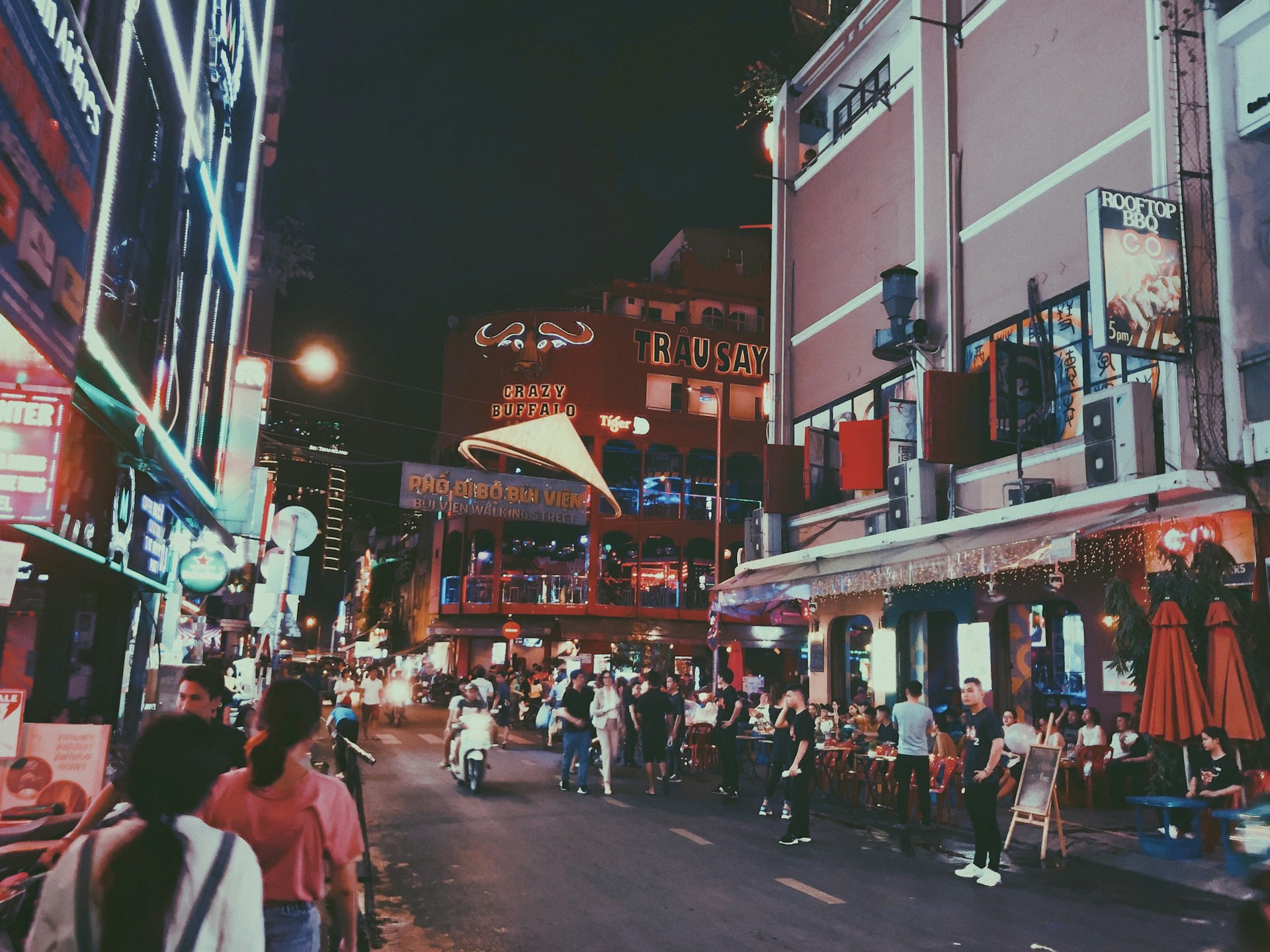 A lively street filled with tourists, where friendly promoters engage with passersby, creating an inviting atmosphere.