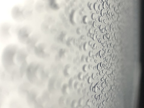 Droplets of water are clustered together on a transparent surface, likely glass, creating a pattern of circles with varying sizes. The image appears to be taken from a close perspective, with a strong emphasis on texture and detail.