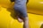 A child wearing a wet grey t-shirt and pants is climbing on a bright yellow inflatable surface. The child's right leg and foot are visible, showing movement and playfulness.