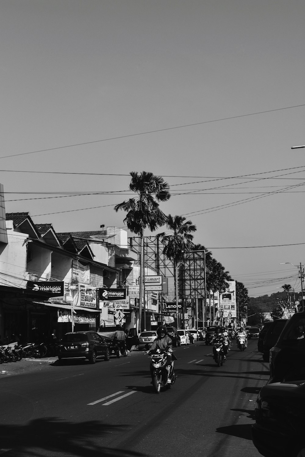 grayscale photo of people riding motorcycles and vehicles parking near buildings and houses