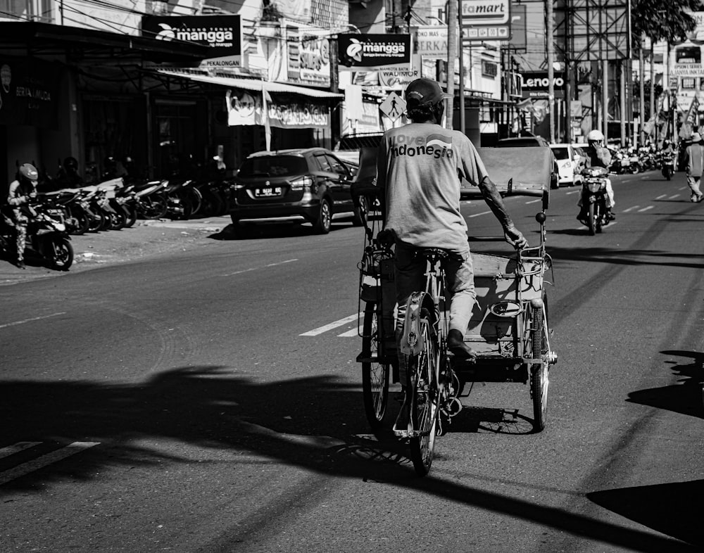 grayscale photography of man pedaling trike