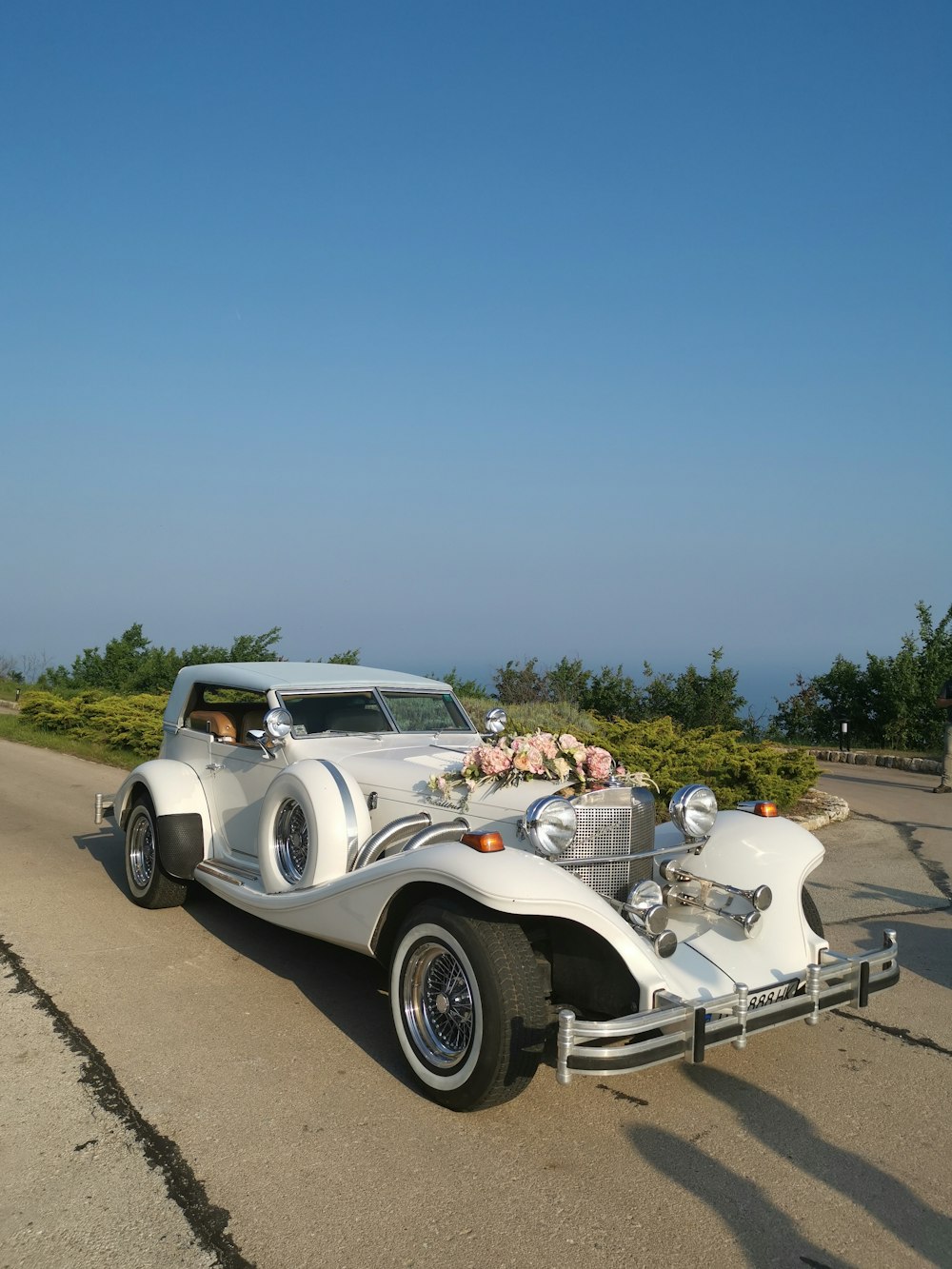 vintage white car with flower decorations in front beside green field