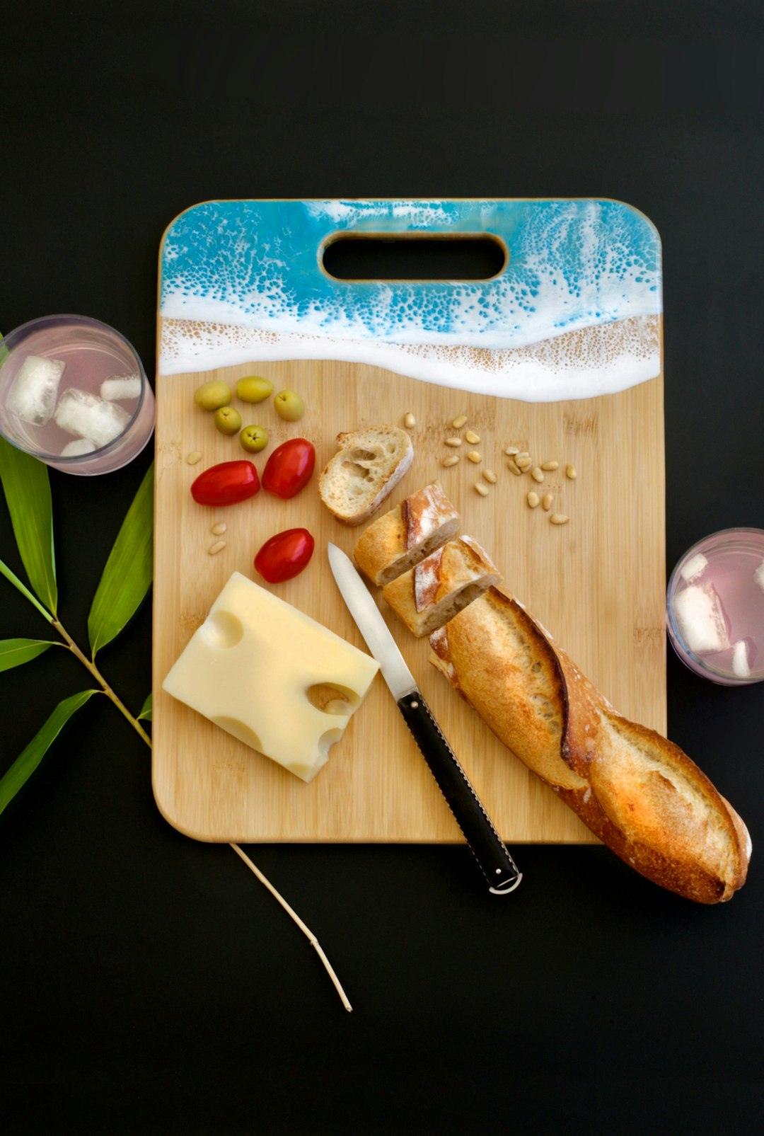 sliced bread near cheese, three red tomatoes, and nuts on wooden chopping board