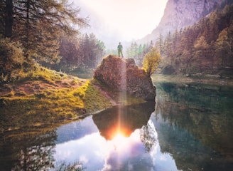 man standing on rock beside lake