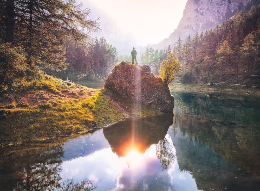 man standing on rock beside lake