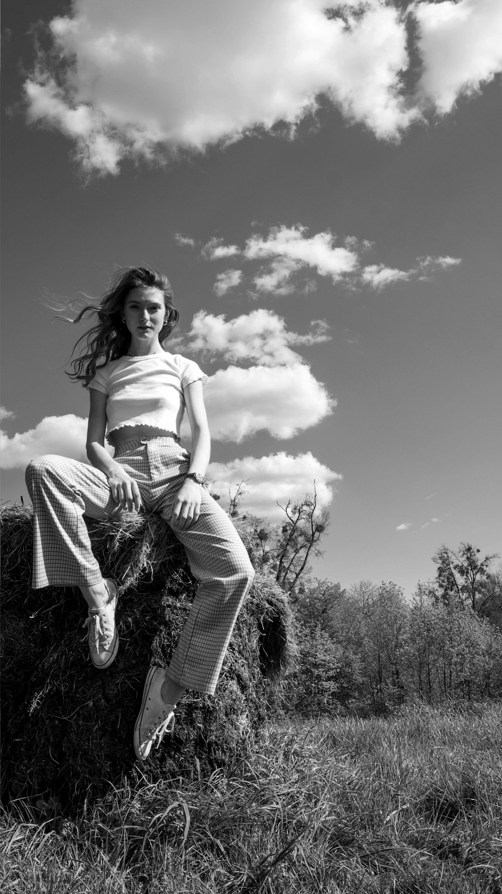 grayscale photography of woman wearing crop top and pants sitting on rock