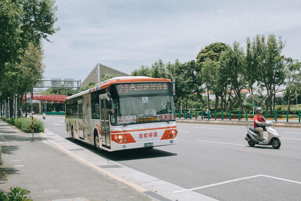 man riding motor scooter near white and orange bus on road viewing trees