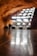 A smooth, reflective floor stretches out towards an abstract structure composed of angled, illuminated panels. The warm, rocky ceiling curves above the scene, suggesting an underground or cave-like environment. The lighting creates a dramatic contrast with the darker surroundings.