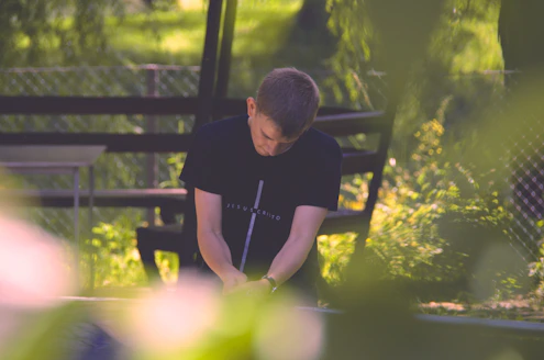 selective focus photography of sitting man wearing black cross graphic shirt