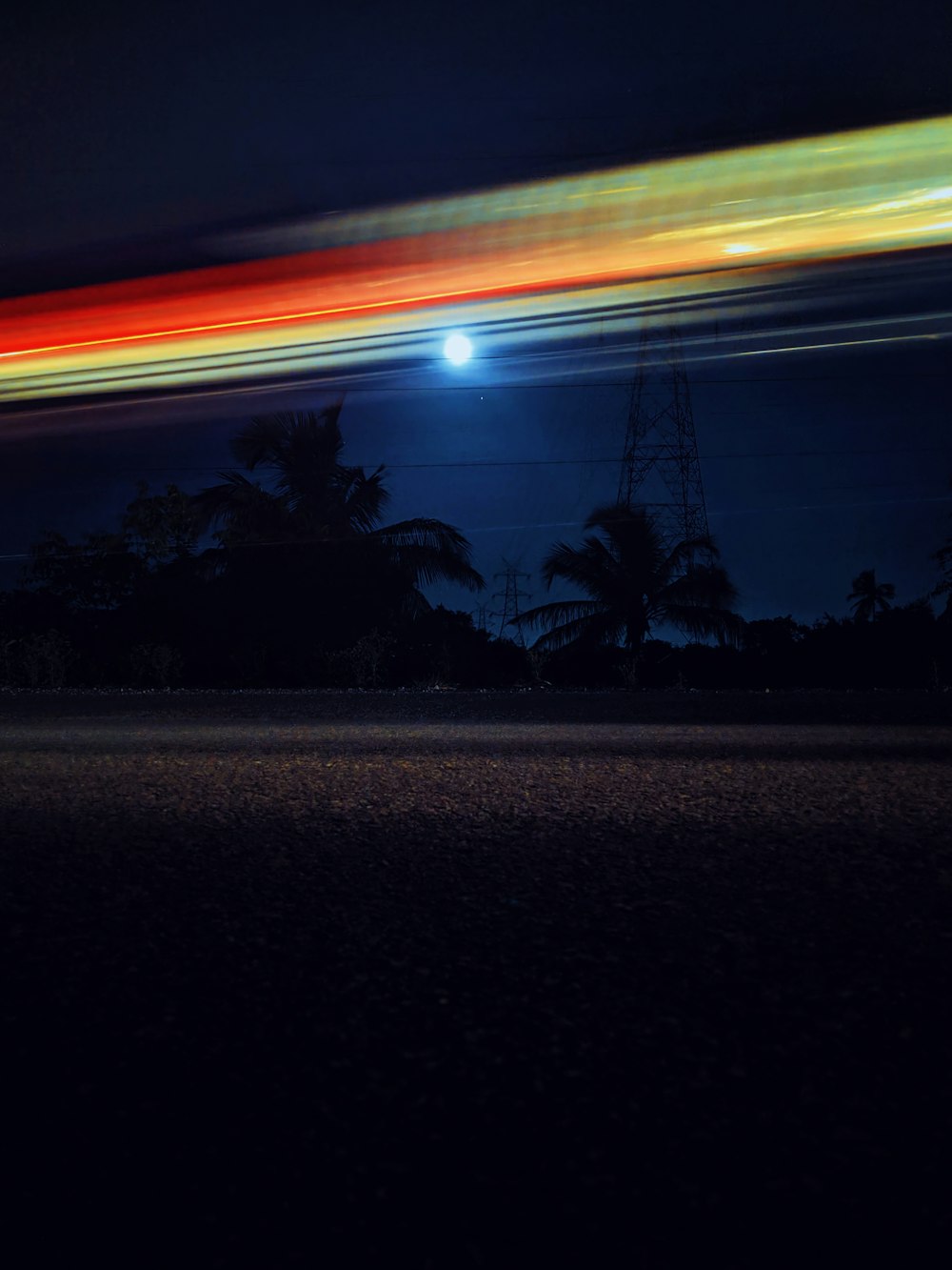 time-lapse photography of road beside trees and transmission tower