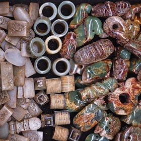 A collection of carved and polished stone artifacts, including rings, rectangular and cylindrical pieces, and various figurines, showcasing intricate designs and a variety of textures.