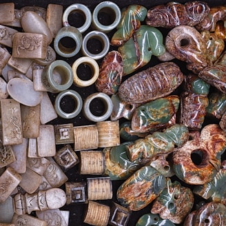 A collection of carved and polished stone artifacts, including rings, rectangular and cylindrical pieces, and various figurines, showcasing intricate designs and a variety of textures.