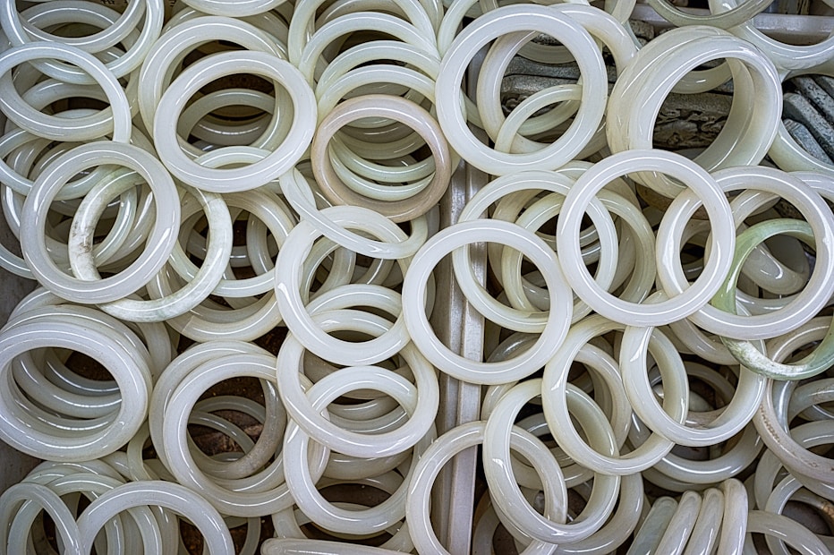 A collection of jade bangles stacked together, showcasing their smooth and polished surfaces with varying shades of pale green and white.