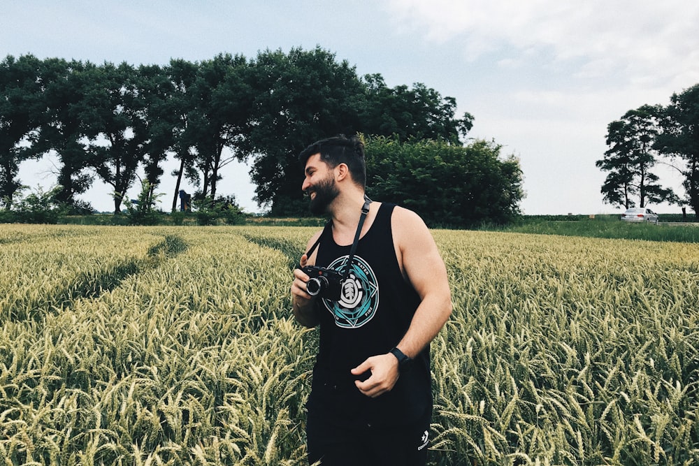 smiling man holding camera standing on whey field