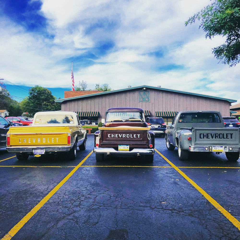 three assorted-color Chevrolet pickup trucks parking near building
