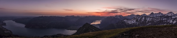 A panoramic view of the snow-capped Himalayas towering over the serene Pangong Lake at sunset.