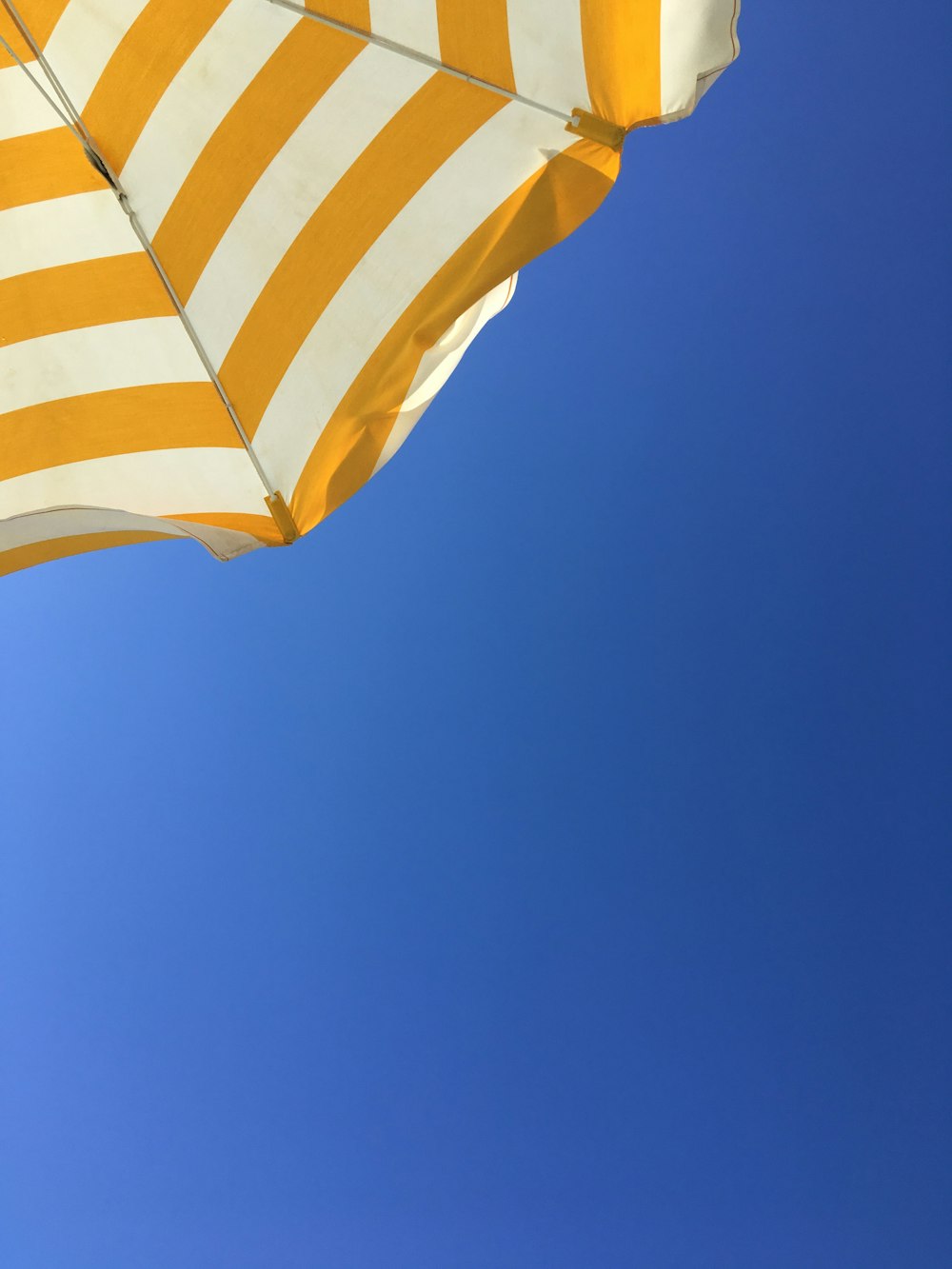 a yellow and white striped umbrella against a blue sky