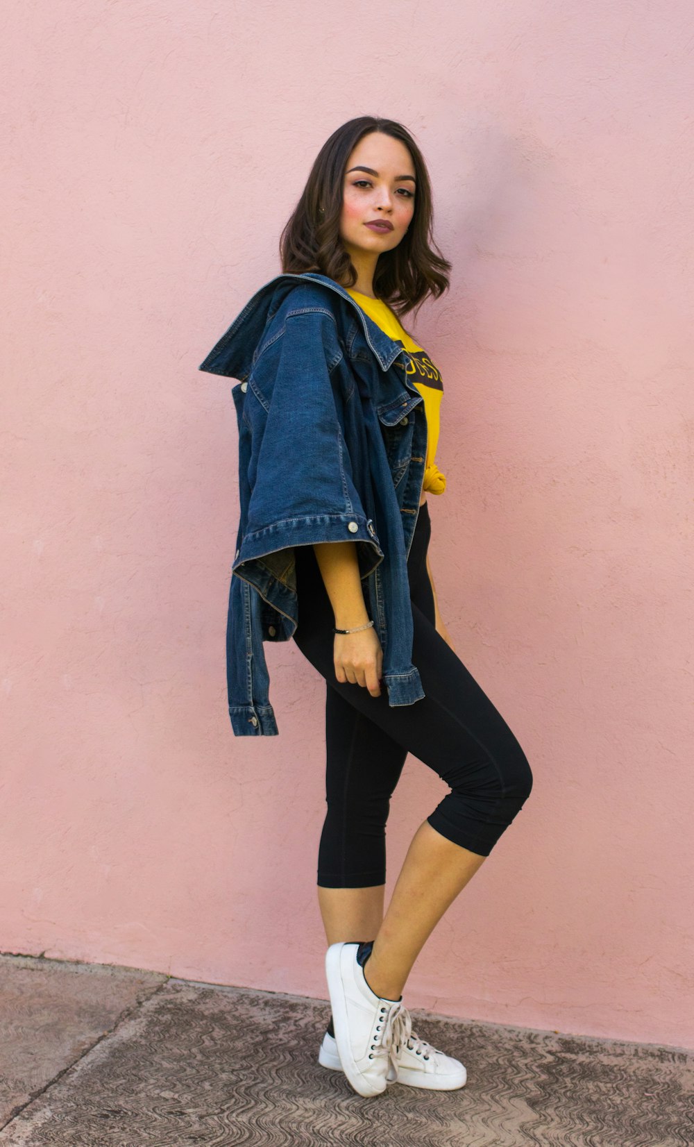 woman wearing blue denim jacket besides pink wall