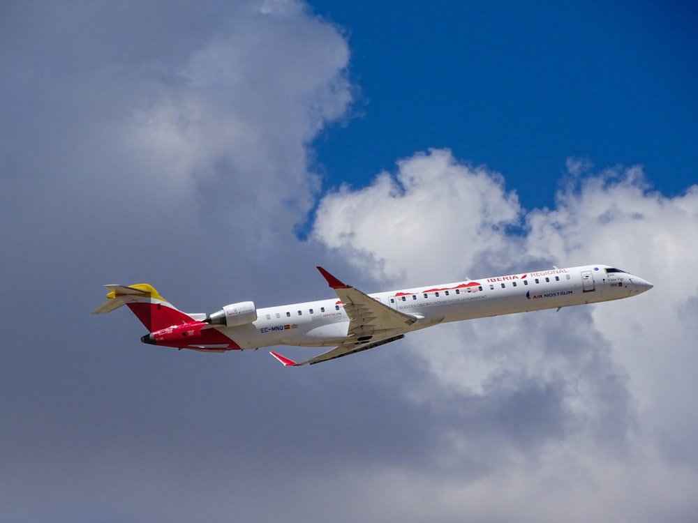 white and red airplane across white clouds