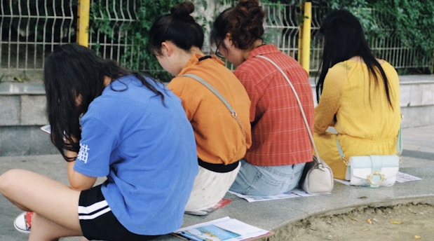 Four diverse girls sitting together under a tree, sharing a book and laughing.