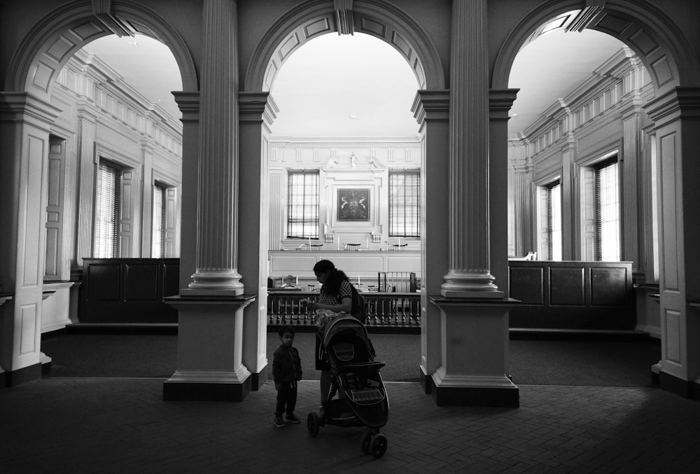 grayscale photo of person standing near stroller and boy
