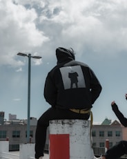 person in black hoodie sitting on concrete post