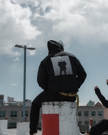 person in black hoodie sitting on concrete post