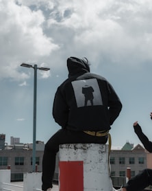 person in black hoodie sitting on concrete post