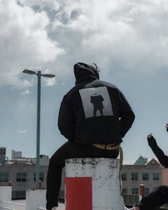 person in black hoodie sitting on concrete post