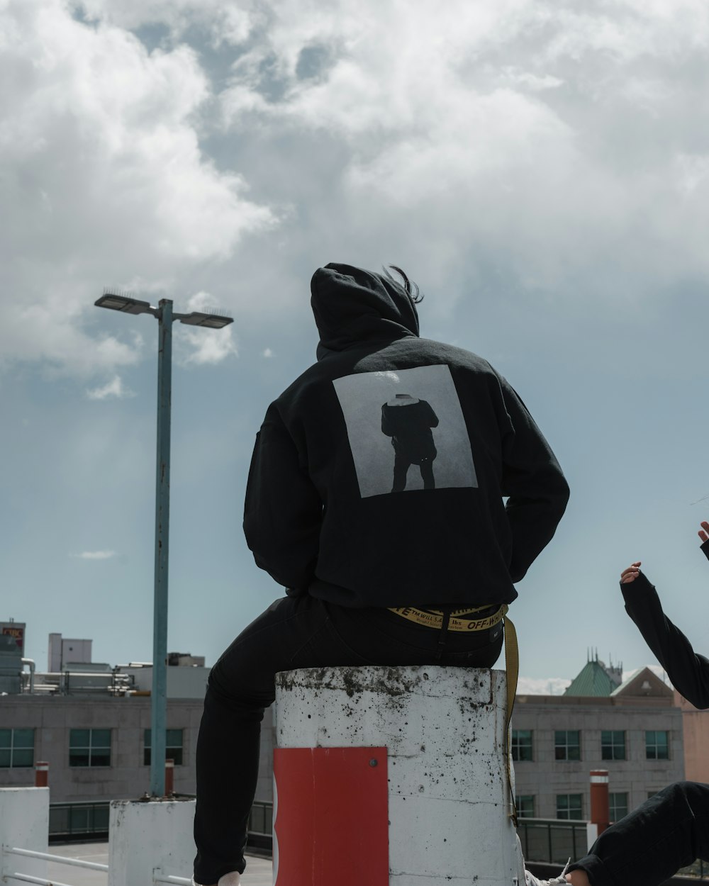 person in black hoodie sitting on concrete post