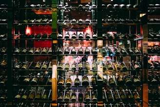 A well-organized wine cellar with multiple rows of wine bottles stored on metal racks. The dim lighting and reflective glass create a cozy and sophisticated ambiance.