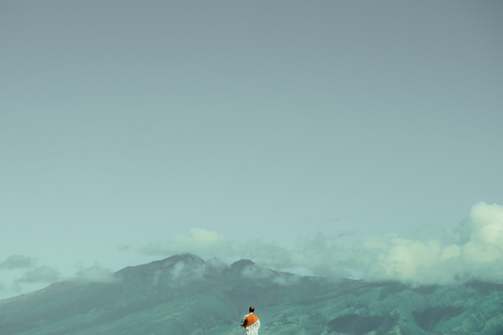 man standing in front on green mountain range during daytime