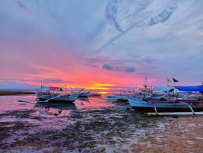 A vibrant sunset over a quiet beach with colorful boats resting on the shore