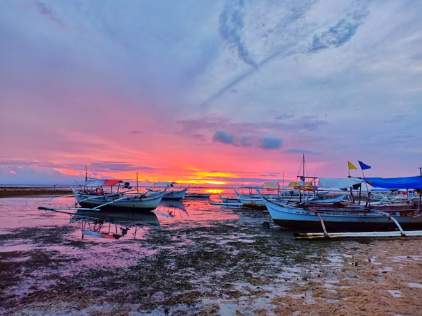 A vibrant sunset over a secluded Philippine island beach with traditional boats anchored near the shore.