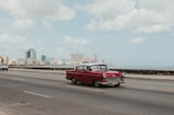A compact red city car driving along a coastal road with the ocean in the background.
