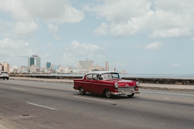 A compact red city car driving along a coastal road with the ocean in the background.