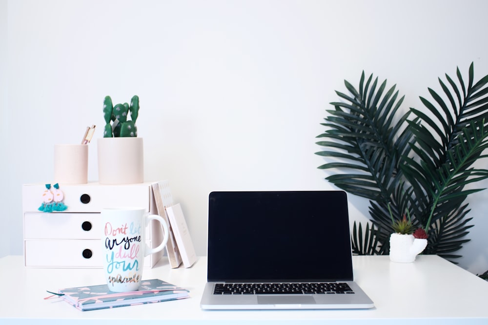 MacBook éteint à côté d’une tasse sur un carnet de notes