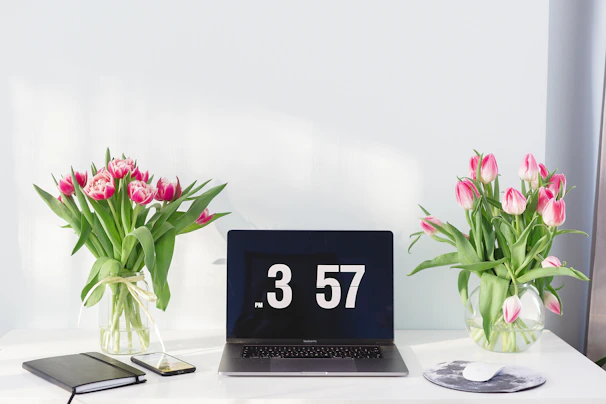 A minimalist desk setup with a notebook, pen, and a small purple flower vase.
