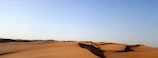 A panoramic view of the Sahara desert dunes under a bright blue sky.