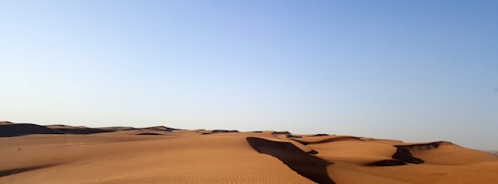 A scenic view of the Moroccan desert with rolling sand dunes under a clear blue sky.