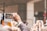 A crowd of people is gathered, with an individual holding up a smartphone to capture the scene. The hand holding the phone is prominently in focus, displaying the live view of a group event. Other people's phones are also visible, suggesting a shared effort to document the moment. The background appears to be an urban setting with architectural elements.