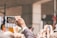 A crowd of people is gathered, with an individual holding up a smartphone to capture the scene. The hand holding the phone is prominently in focus, displaying the live view of a group event. Other people's phones are also visible, suggesting a shared effort to document the moment. The background appears to be an urban setting with architectural elements.