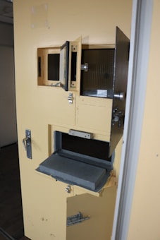 A yellow door with multiple small compartments and latches, featuring a sliding tray mechanism presumably for secure transactions or communications.
