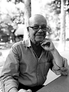 A smiling senior enjoying a puzzle book at a kitchen table, surrounded by vintage memorabilia from the 1950s.