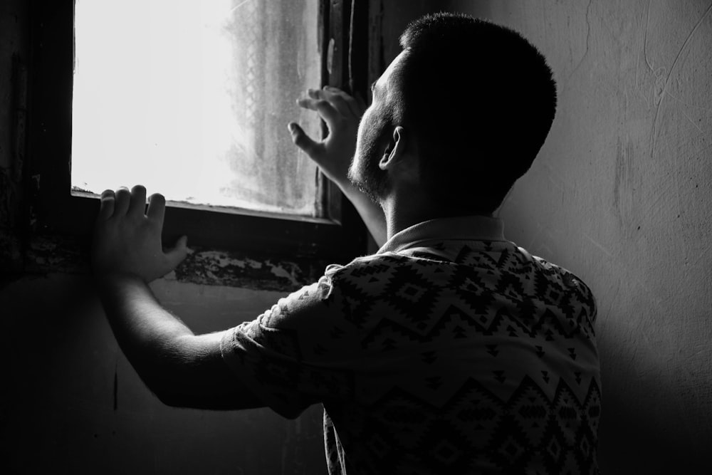 greyscale photo of man reaching window