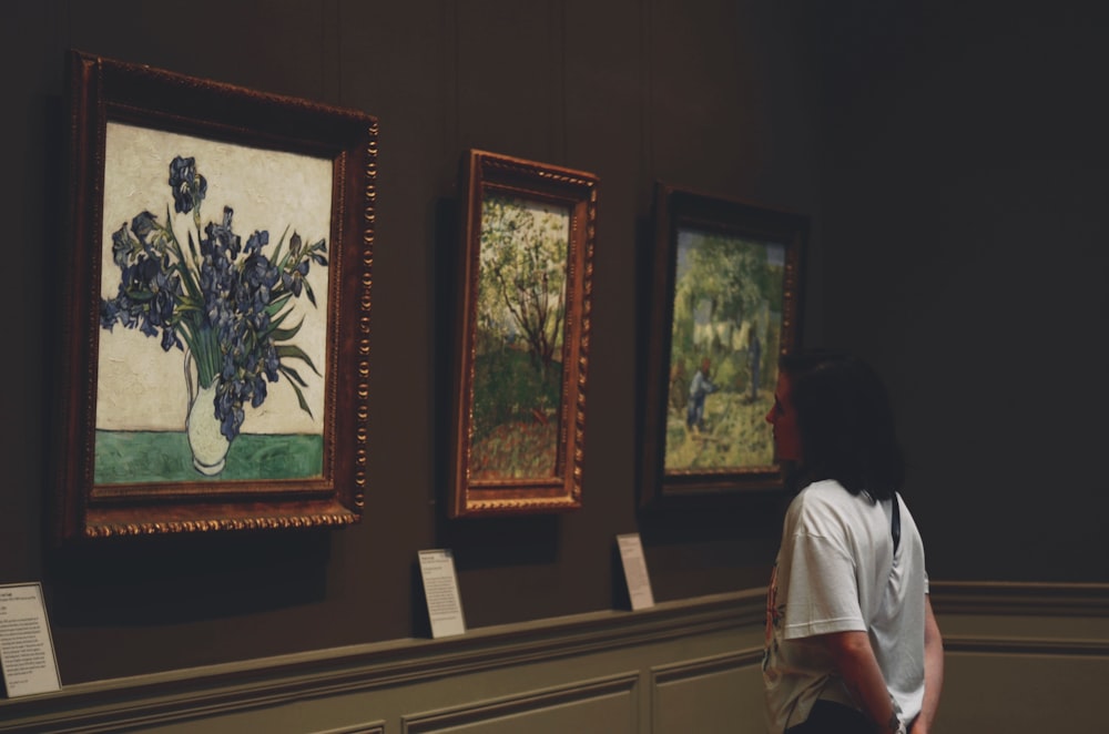 a woman looking at paintings on display in a museum