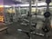 A well-equipped gym with various weightlifting equipment including benches, barbells, dumbbells, and weight racks. There are mirrors on the walls and rubber flooring. The lighting is bright yet soft, and the gym appears clean and organized.