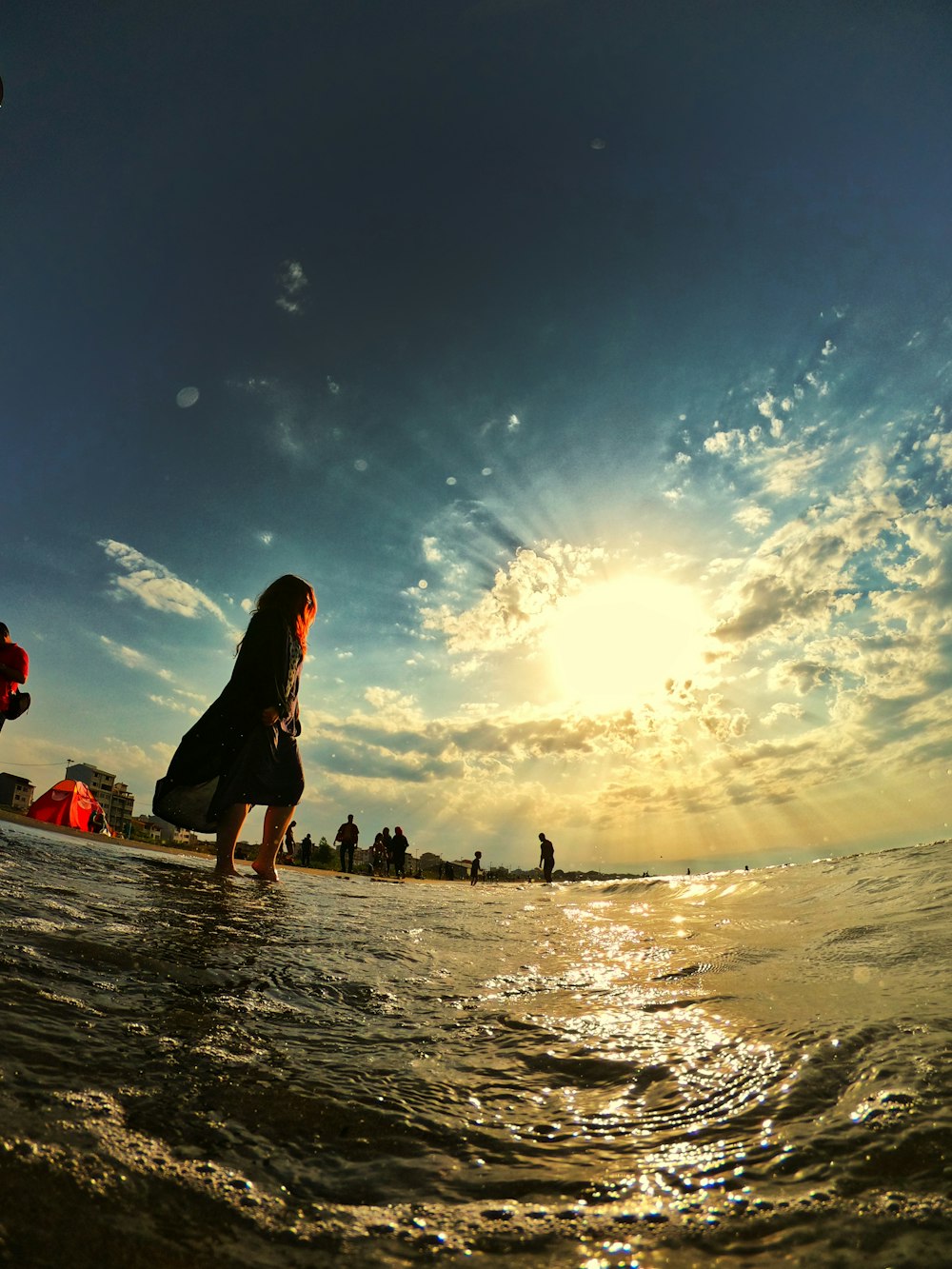 woman wearing black dress on body of water across sun and clouds