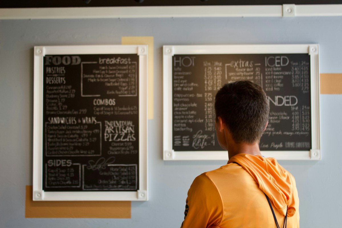 Cliente de costas lendo os cardápios em quadro-negro na parede
